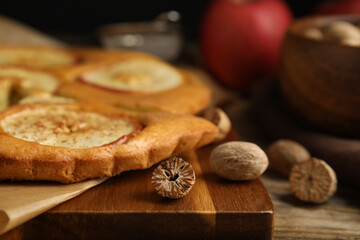 Nutmeg seeds and tasty apple pie on wooden table, closeup