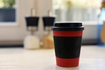 Hot coffee in takeaway paper cup on wooden table at cafe, space for text