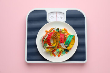 Scales with weight loss pills and measuring tape on pink background, top view