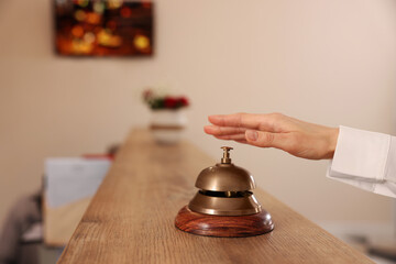 Woman ringing hotel service bell at wooden reception desk, closeup