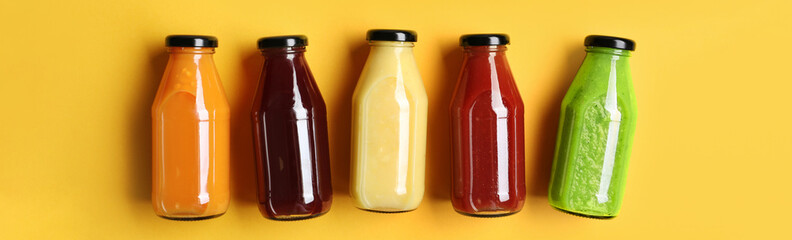 Bottles with delicious colorful juices on yellow background, flat lay with space for text. Banner design