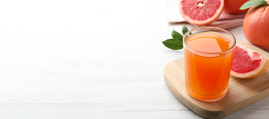 Tasty freshly made grapefruit juice on white wooden table, space for text. Banner design