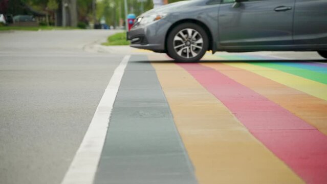 Cars drive over a rainbow cross-walk in slow motion with rollerbladers in the background.