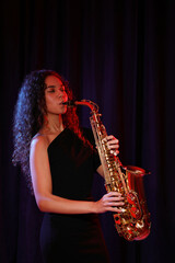 Fototapeta na wymiar Beautiful African American woman playing saxophone on dark background