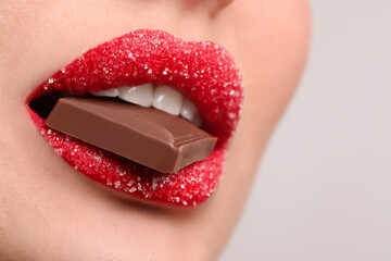 Closeup view of young woman with beautiful lips covered in sugar eating chocolate on light grey background