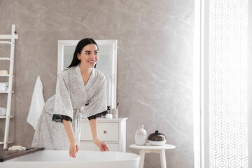 Beautiful young woman in silk robe near bathtub at home