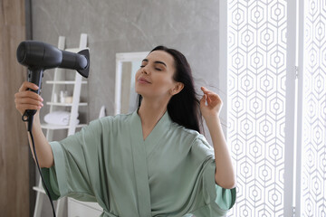 Beautiful young woman using hair dryer in bathroom