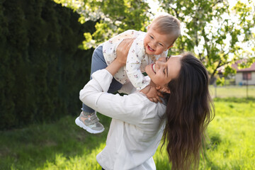 Happy mother playing with her cute baby in park on sunny day