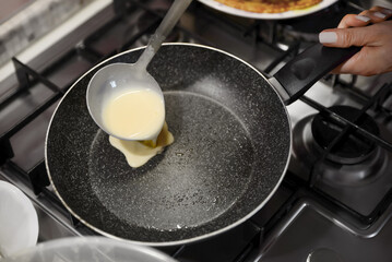 Woman pouring crepe batter onto frying pan in kitchen, closeup