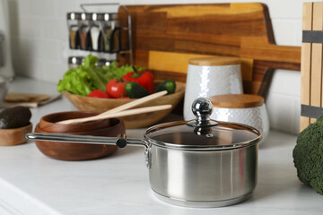 Metal saucepan, other cooking utensils and fresh vegetables on countertop in kitchen