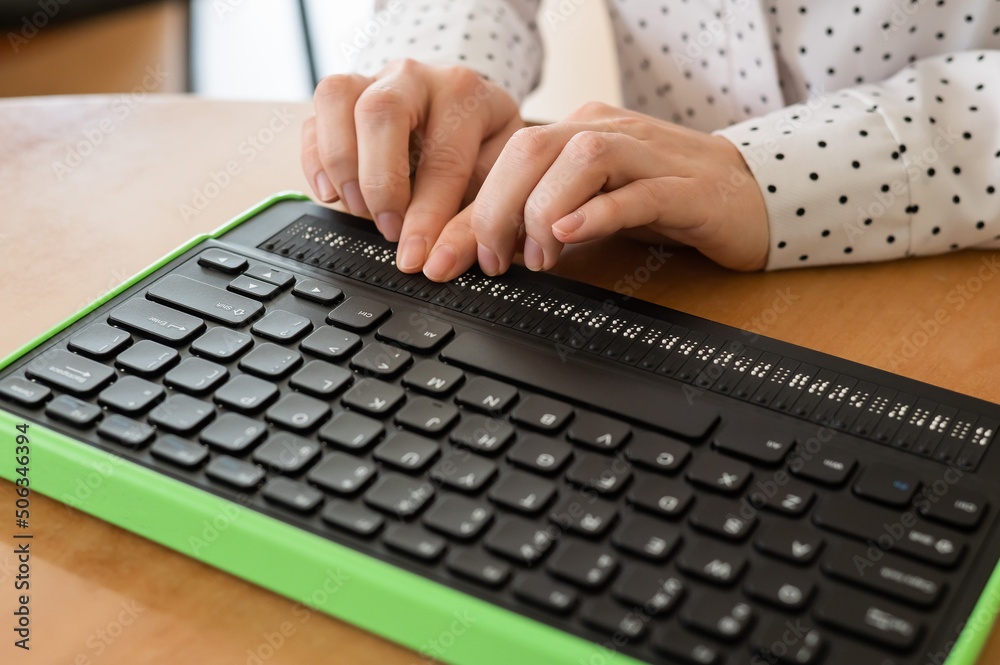 Wall mural a blind woman uses a computer with a braille display and a computer keyboard. inclusive device.