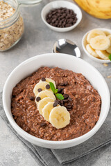 Chocolate oatmeal porridge with banana and chocolate chips on top in a white bowl. Healthy breakfast. Copy space.