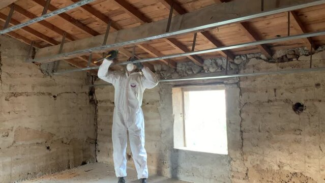 Wood Boring Insect Treatment - Worker In PPE Suit And Mask Scraping The Wood Beam Of House Damaged By Wood-boring Insects. - static