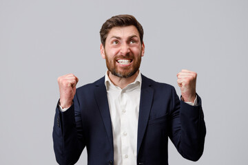 Happy joyful businessman wearing suit doing winner gesture clenching fists 