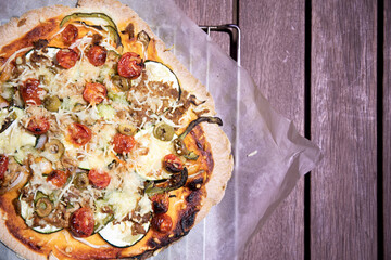 A top view of hot Italian pizza on a wooden table background. Whole colorful pizza with vegetables. Copy space.