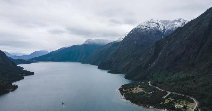 Aerial hyperlapse of Tagua Tagua Lake, southern Chile. Mountains with snow on top, cloudy day. Ferry passing by the lake.