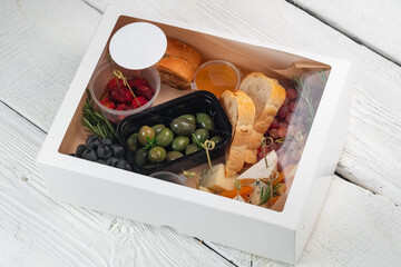 A gift set of snacks for wine - cheese, grapes, tomatoes, honey, olives in a delivery box. appetizers on a wooden background