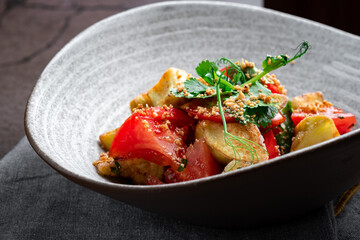 Fried zucchini slices with crispy crust with tomatoes, herbs and nuts. Vegetarian dish on a grey plate, close up