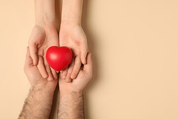 Couple holding red heart on beige background, top view. Space for text