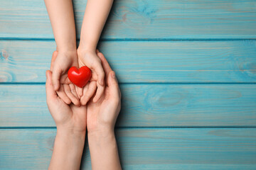 Woman and kid holding red heart in hands at light blue wooden table, top view. Space for text