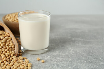 Glass with fresh soy milk and grains on grey table. Space for text