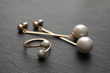 Elegant golden ring and earrings with pearls on black table, closeup
