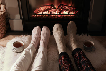 Couple in knitted socks near fireplace at home, closeup of legs