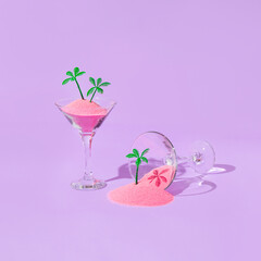 Summer tropical creative layout with martini cockatil glasses with pink sand and palm trees figurines on pastel purple background. 80s, 90s retro fashion aesthetic summer concept. Pop art idea.