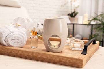 Aroma lamp, bottle of oil, rolled towel and candles on wooden tray indoors