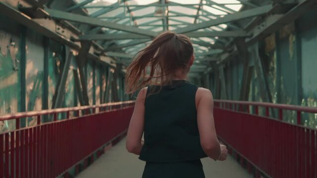 Back view of the receding figure of a beautiful girl running across the bridge