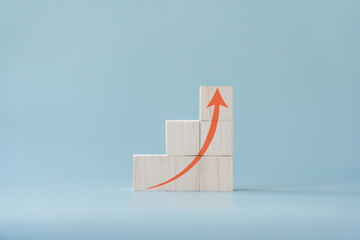 Red arrow going up on wooden blocks and light blue background. Concept of growing or improving.