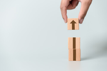 Brown arrow going up on wooden blocks and light blue background. Concept of growing or improving in...