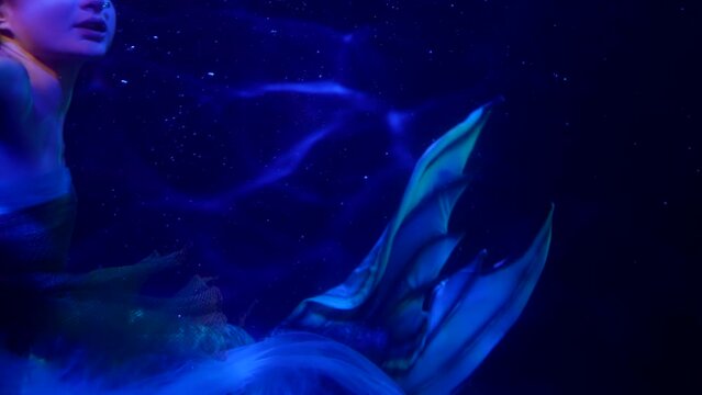 a mermaid waves tail in the dark water. blue light. close-up