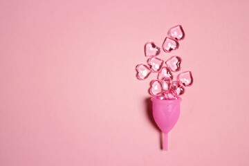 Menstrual cup with decorative hearts on pink background. Women's health, hygiene concept.