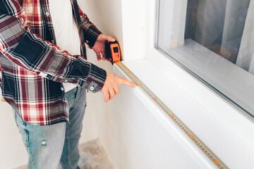 worker builder measures the window sill with a construction tape, close-up