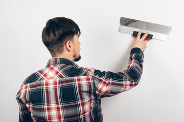 male builder puttying a white wall, view from the back