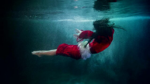 a woman with dark long hair in a red suit with white fur hovers horizontally and bends legs in blue water. the general plan