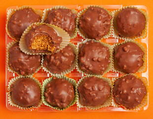 Tasty chocolate candy ball shapes with filling and nuts, on orange background. Fill the entire frame, rectangle tray