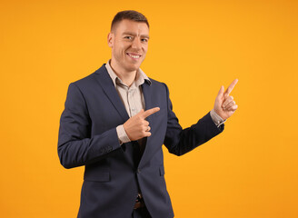 smiling man in suit points two fingers to the side on yellow background with copy space