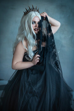 A Gothic beauty, a dark evil queen in a black fluffy dress with chess pieces. Plus size model in a crown, in the role of a dark queen with white hair and professional dark makeup. Artistic photography