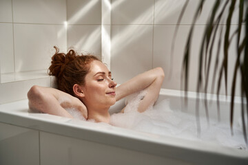 Young redhead woman taking a bath with eyes closed