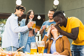 Moments of celebration in the family, young adoptive son covers his mother’s eyes to make a surprise, picnic in the back yard, extended family party concept