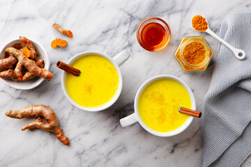 Obraz na płótnie Canvas Turmeric tea, latte, golden milk in cups with cinnamon and fresh roots turmeric. Marble background. Top view.