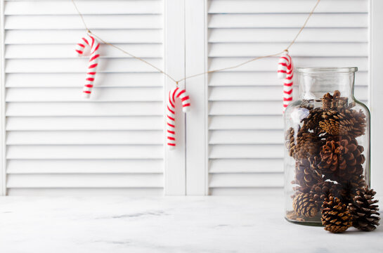 Christmas, New Year decorations, candy canes, cones in a glass jar. White wooden blindes background. Copy space.