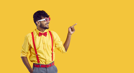 Happy young ethnic guy shows something on yellow copy space background. Cheerful Indian man in...