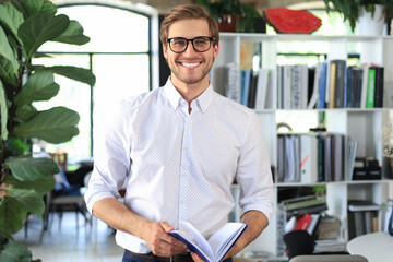 Handsome young businessman standing in modern office. - obrazy, fototapety, plakaty