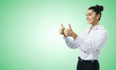 Like concept with happy young businesswoman in white shirt holding thumbs up on light green wall...