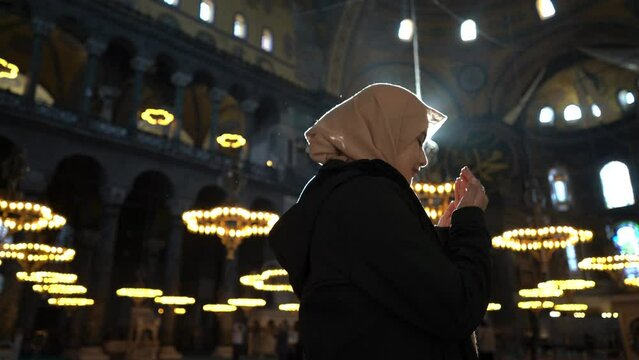 Asian muslim woman in scarf praying with her hands raised in Hagia Sopia Mosque
