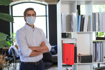 Naklejka na ściany i meble Young businessman in medical mask standing in modern office.