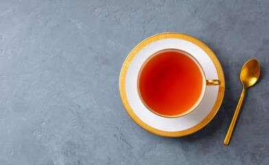 Tea in white cup with gold rim. Grey background. Copy space. Top view.